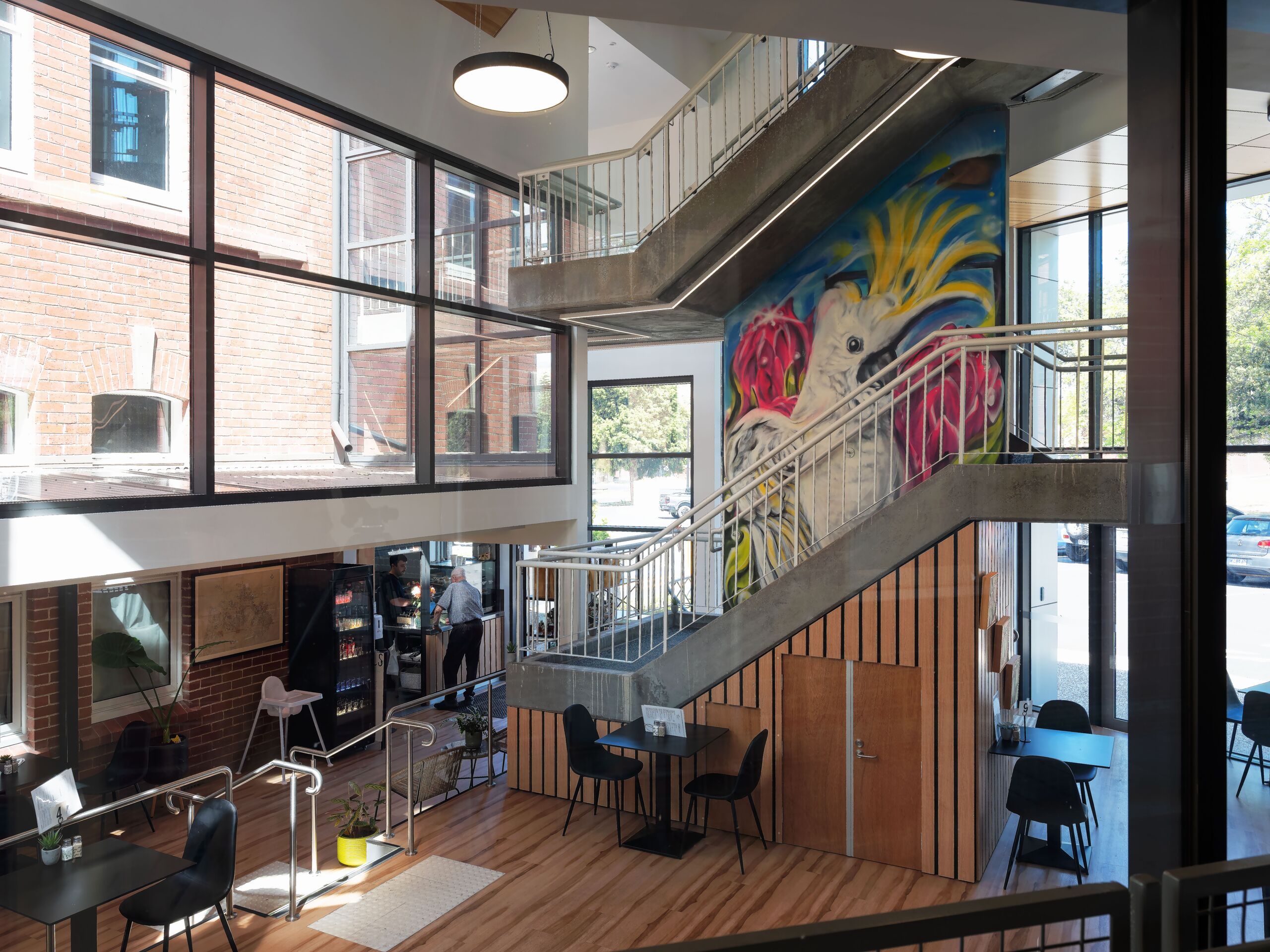 Double-height glazed atrium with mural, stair and café seating linking the two heritage buildings