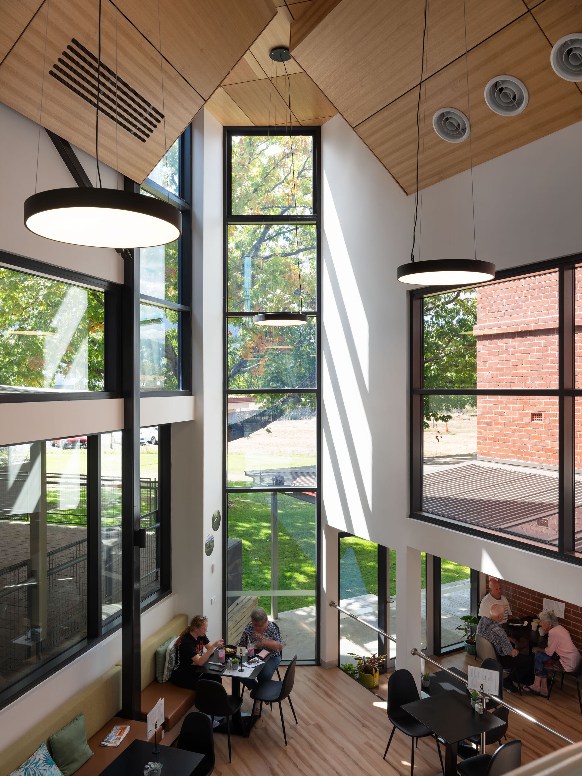 Tall atrium windows and timber-lined ceiling above café seating