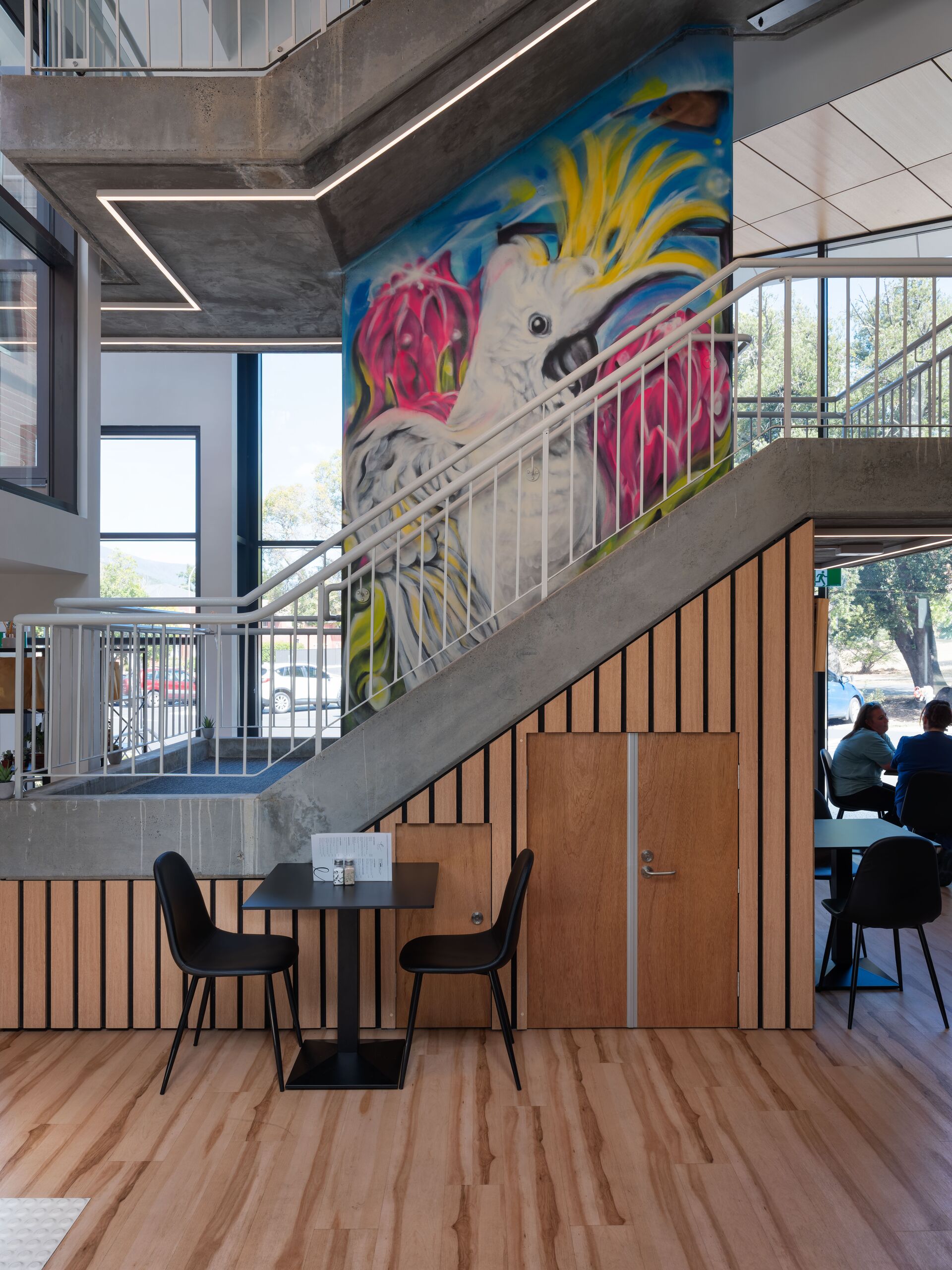 Atrium stair and colourful bird mural above café tables