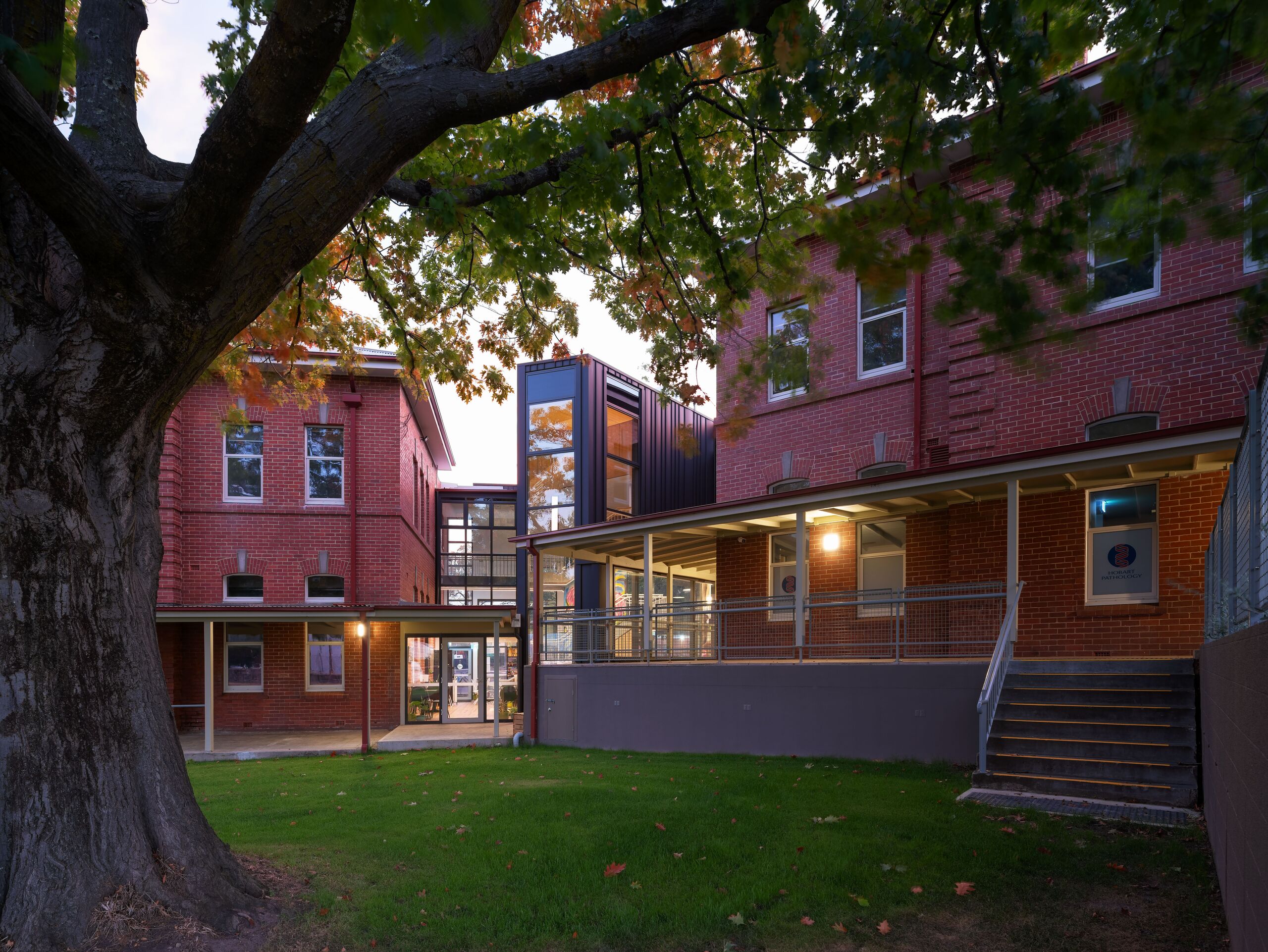 Heritage buildings and atrium at dusk beneath a mature tree, Willow Court, New Norfolk