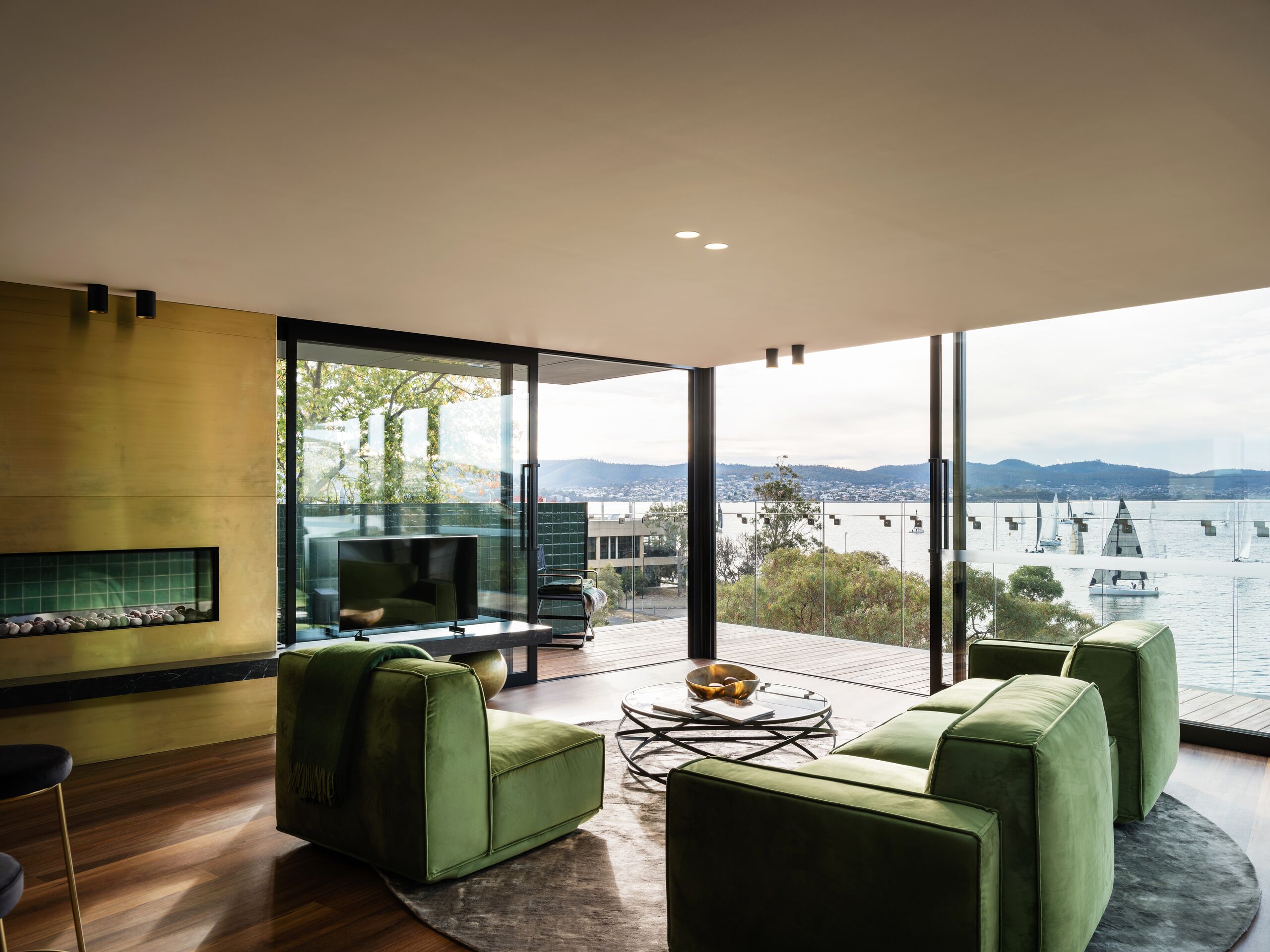 Living room with green lounge chairs, brass fireplace wall and water views