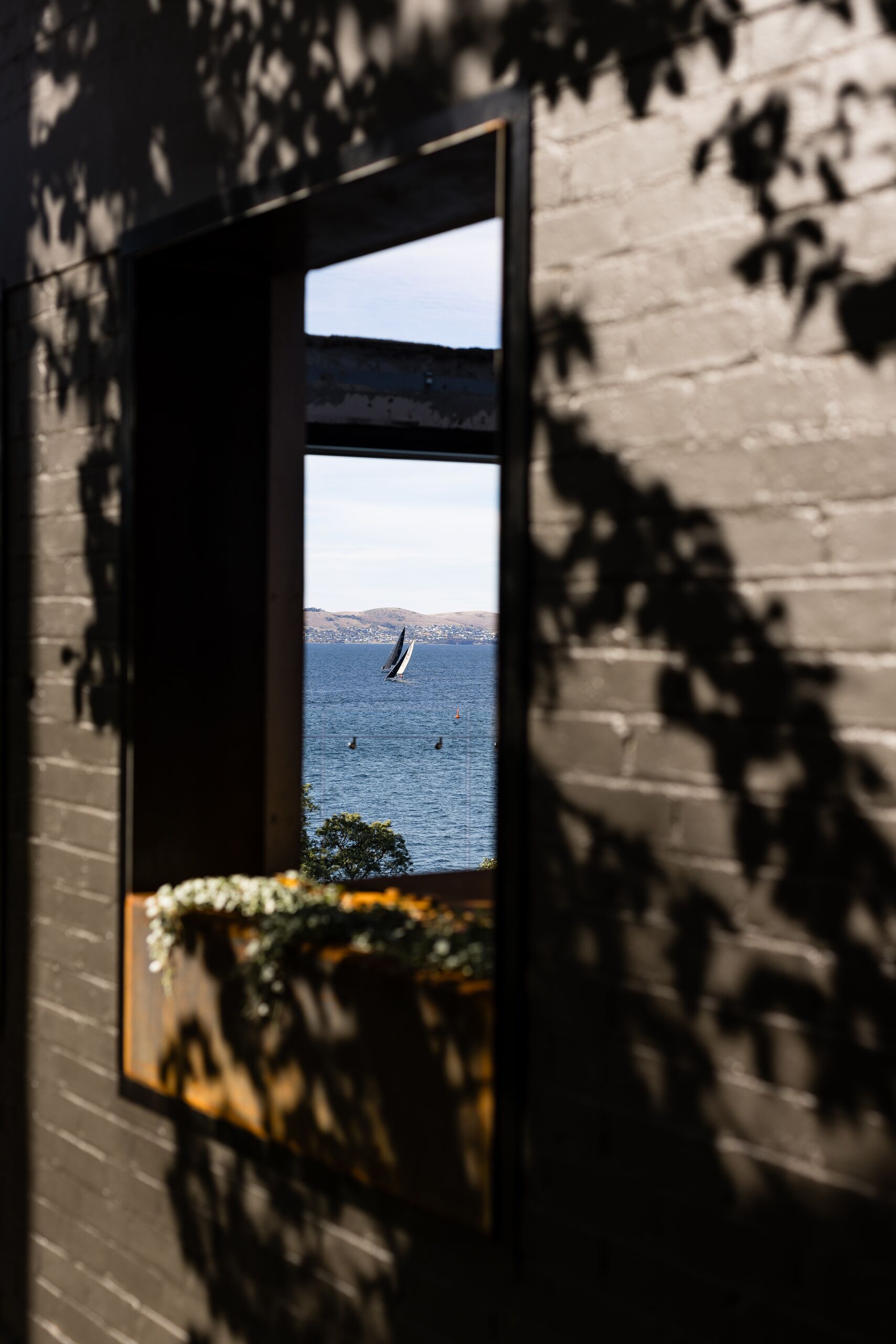 Window in a painted brick wall framing a yacht on the Derwent River