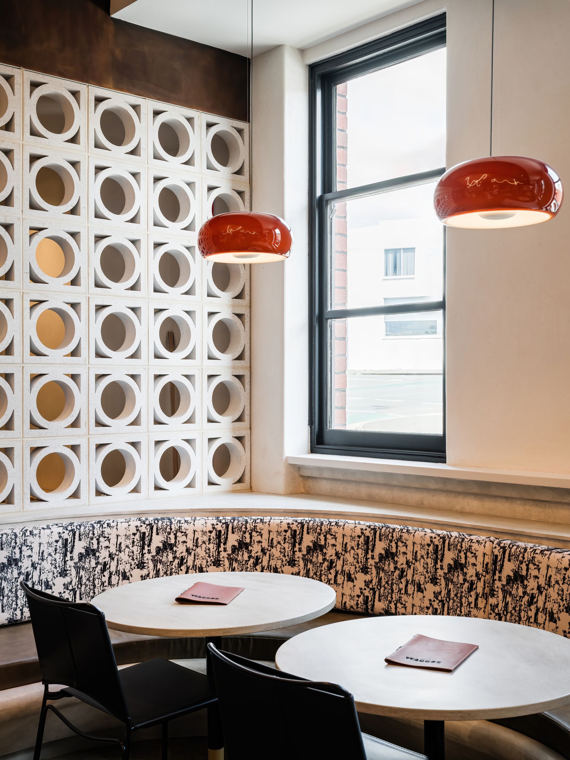 Banquette seating beside a breeze-block screen under red pendant lights