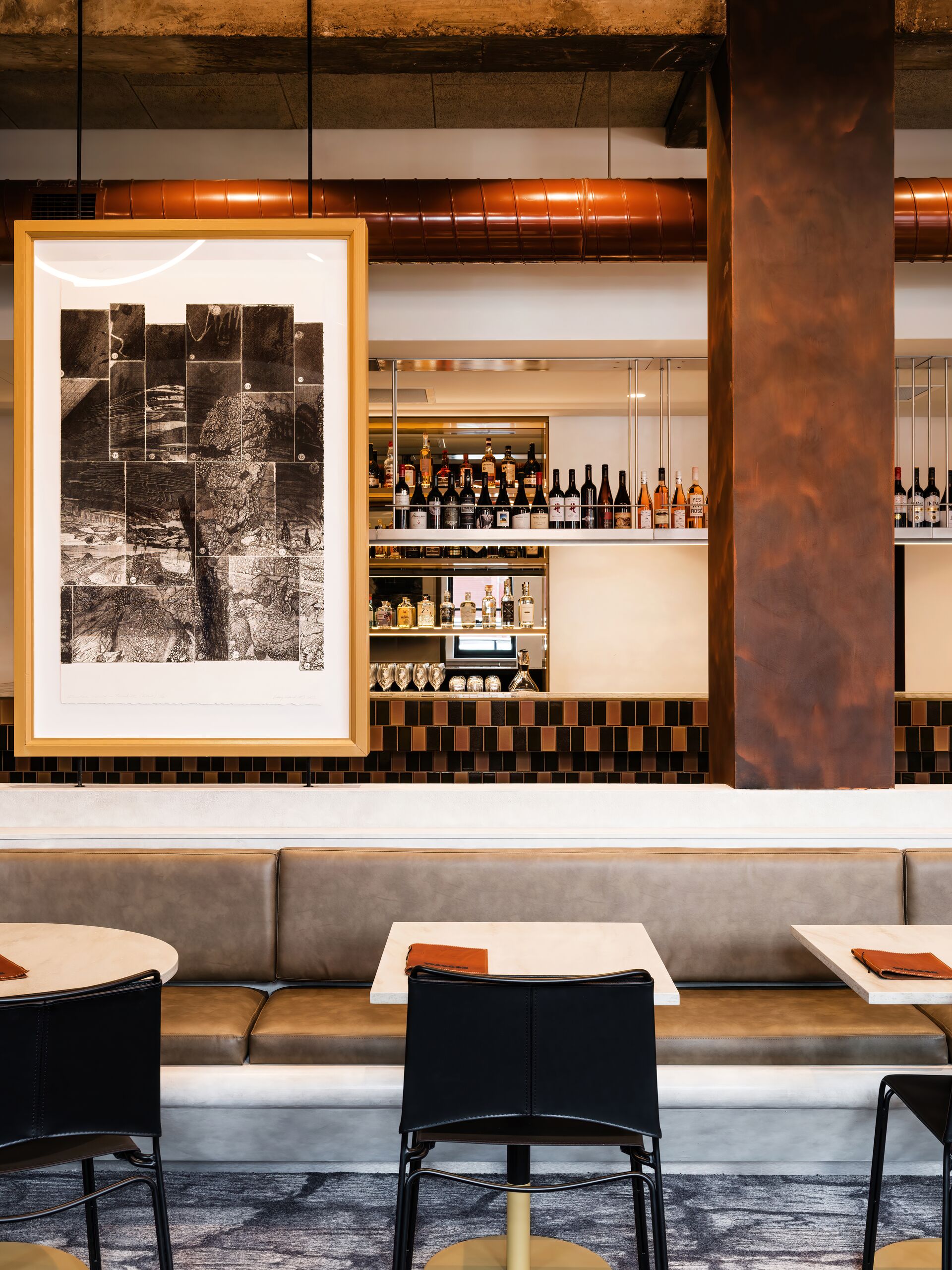 Upholstered banquette with framed artwork and marble tables, bar beyond