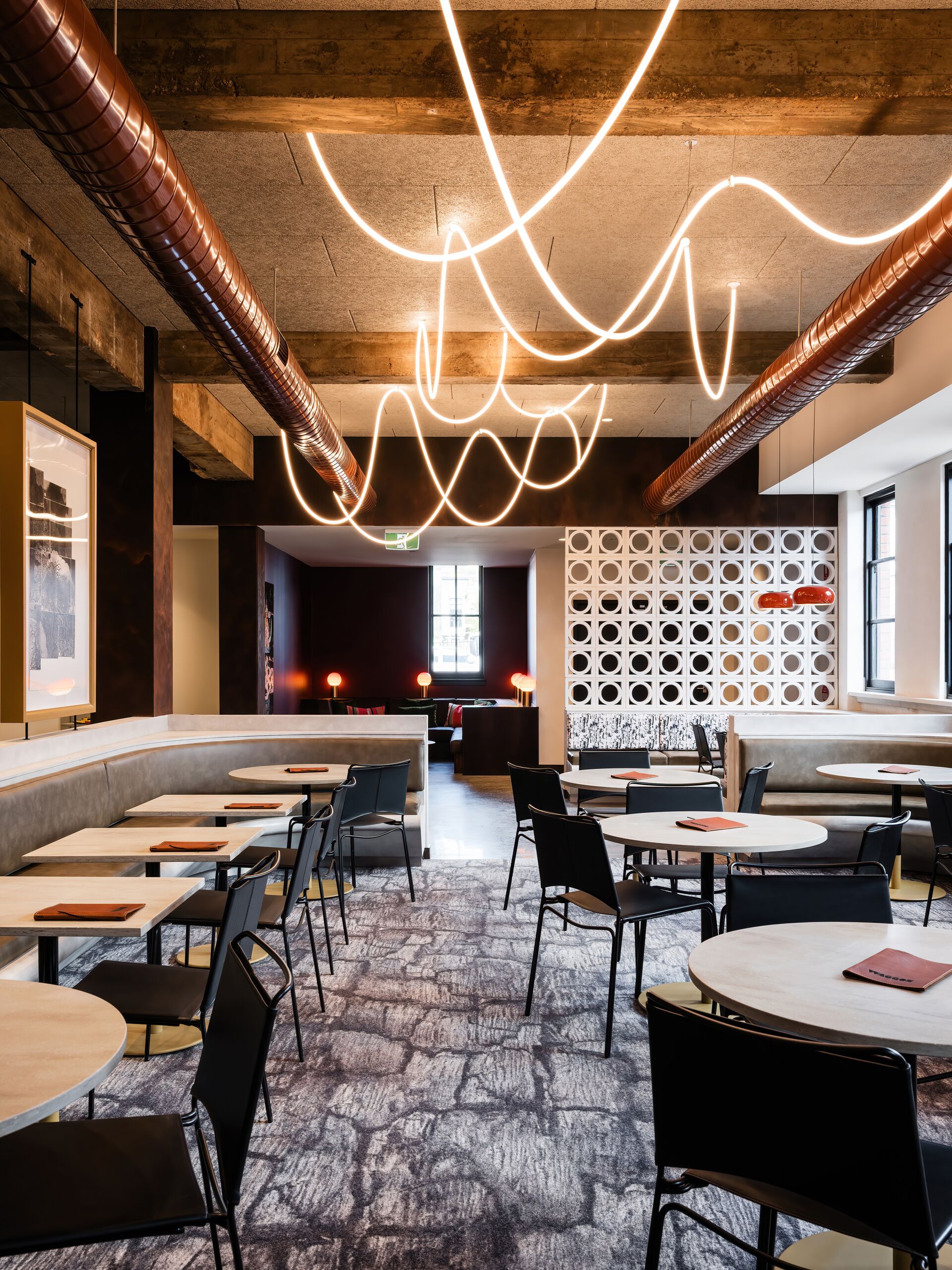 Dining room beneath sculptural neon lighting and the exposed ceiling structure