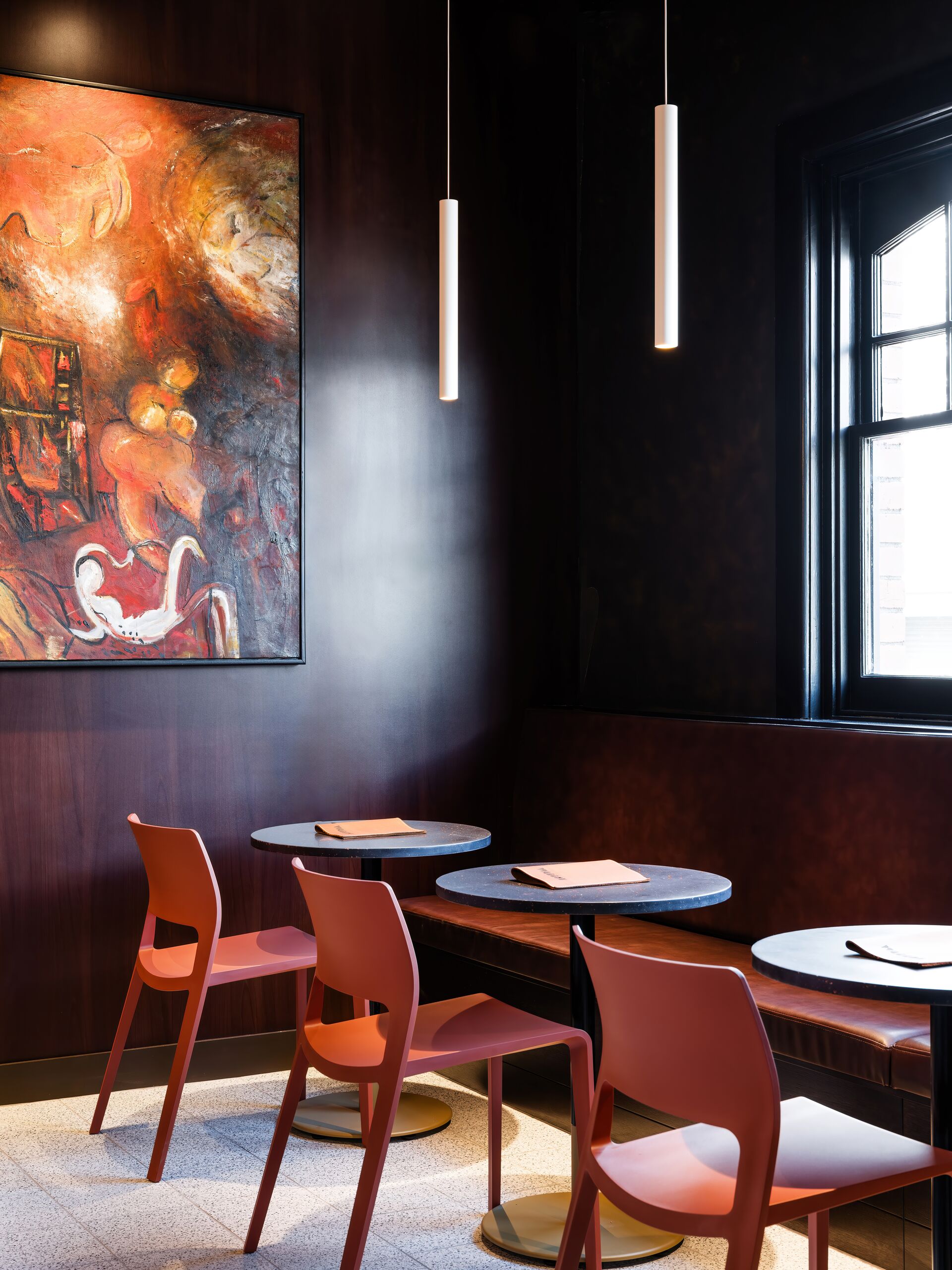 Dining room with dark timber walls, orange chairs and a large painting